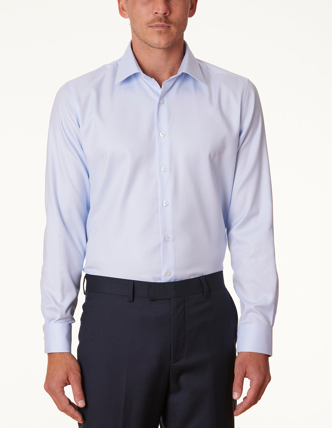 Man wearing a light blue dress shirt and dark pants on a white background